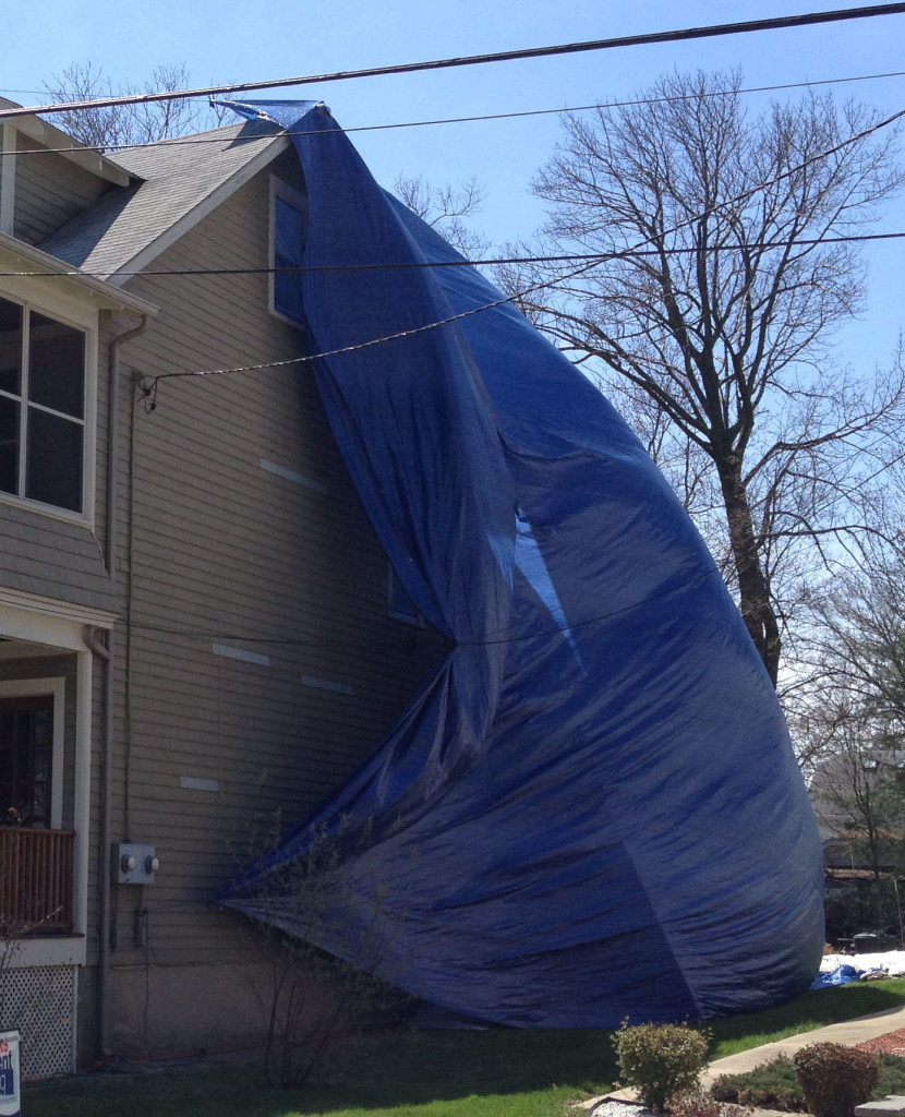 A tarp from roofline to the ground helps contain paint dust that may contain lead.